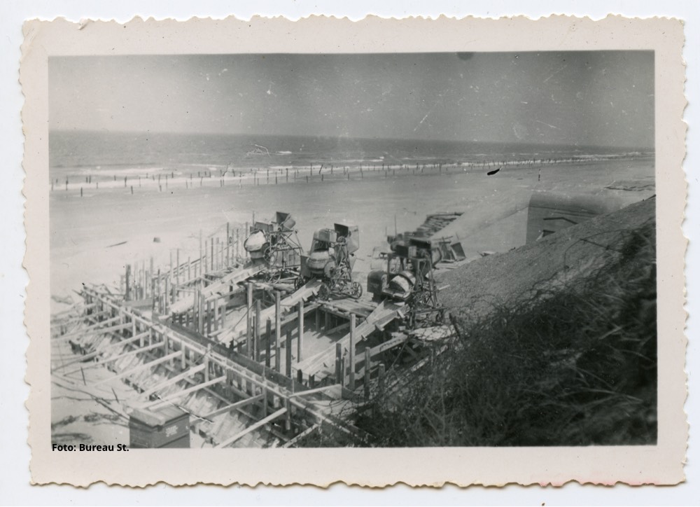 Drie cementmolens en een berg zand bij Castricum aan Zee. Daarachter staat een splinternieuw gebouwde geschutsbunker van het type 667. In de vloedlijn zijn houten palen als strandversperringen zichtbaar. - Foto: J. Rijpsma.